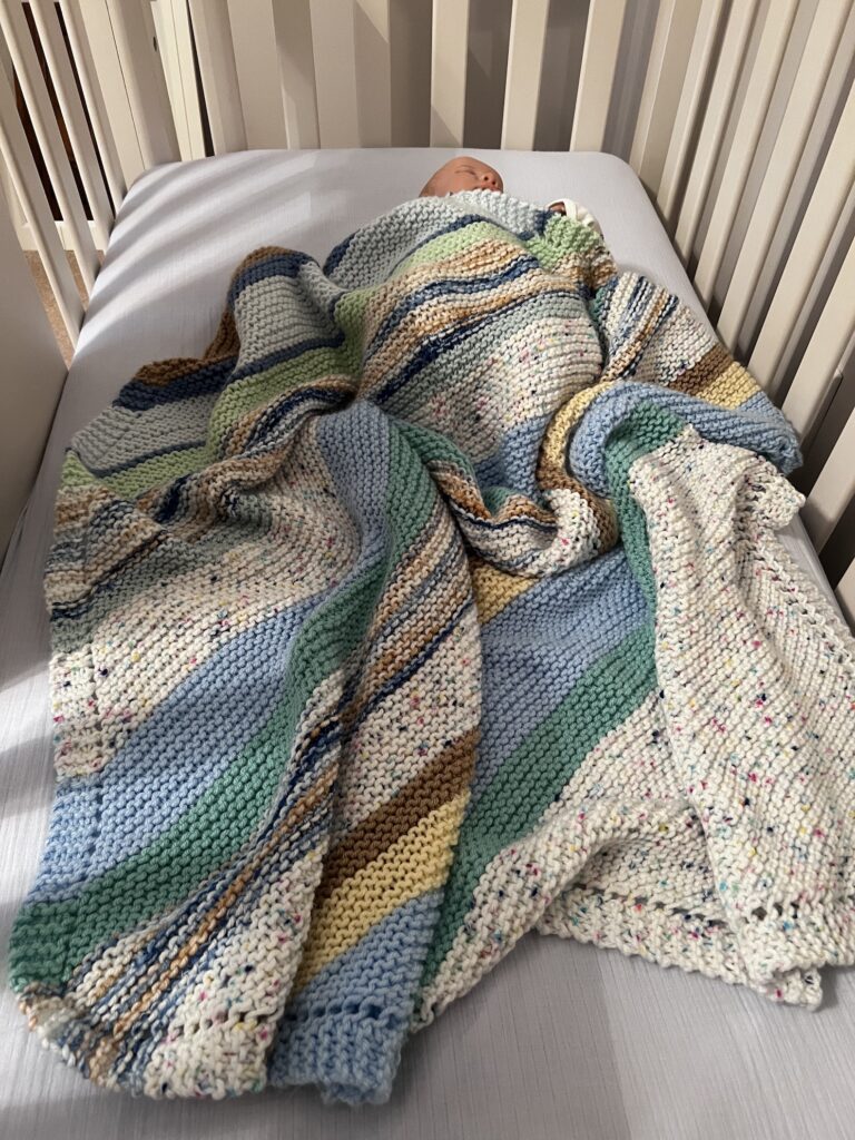 striped handknit blanket covering a baby sleeping in a crib