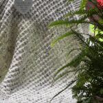 Ivory and tweed textured baby blanket on a red wood bench framed by a fern