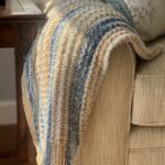 blue and tan hand knit baby blanket draped on a couch