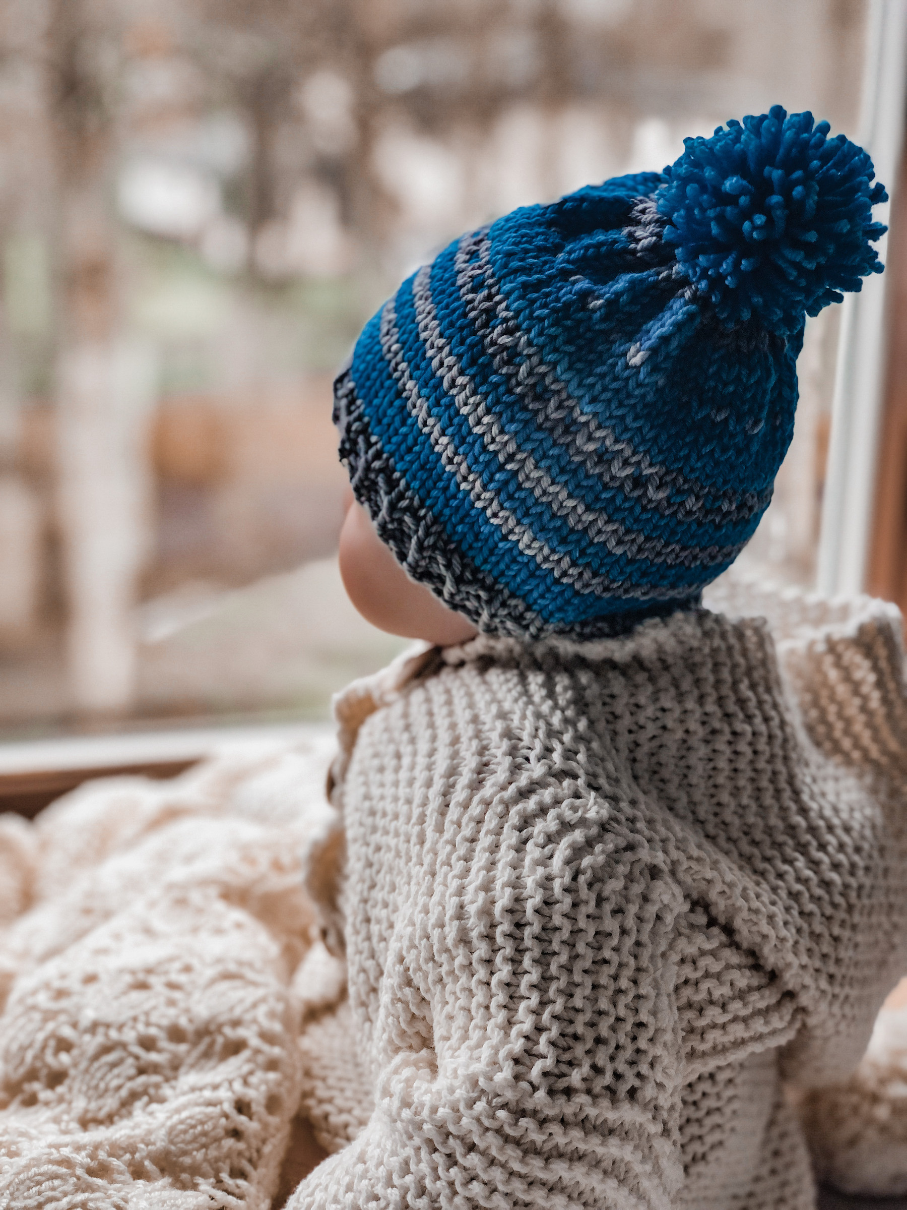 baby with blue hat looking out window