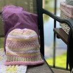 colorful pink hat next to a purple bag with lake in background