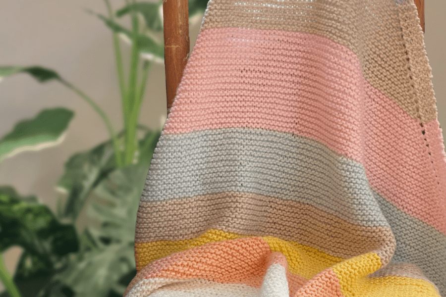 striped knit baby blanket on chair in front of plant