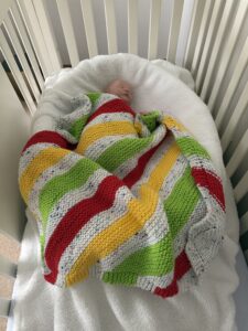 sleeping baby covered by colorful knit blanket in their crib