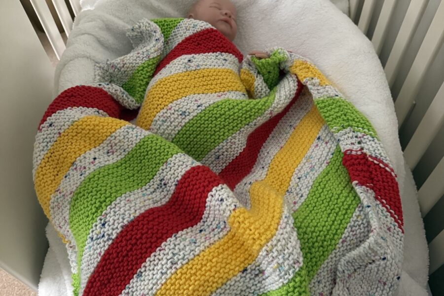 sleeping baby covered by colorful knit blanket in their crib