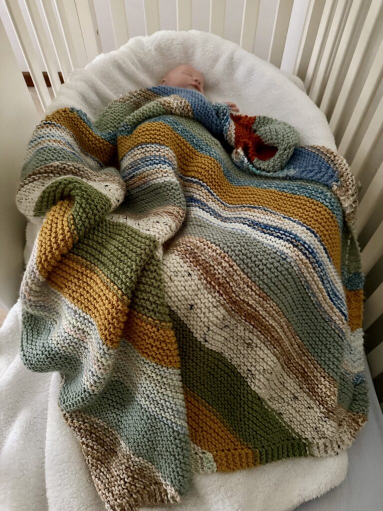 striped baby blanket draping baby in crib