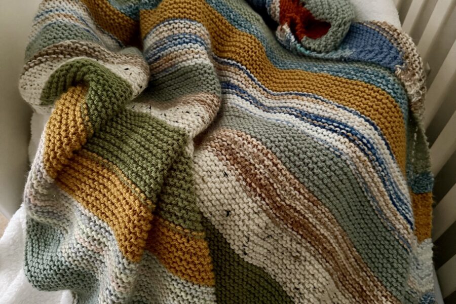 striped baby blanket draping baby in crib