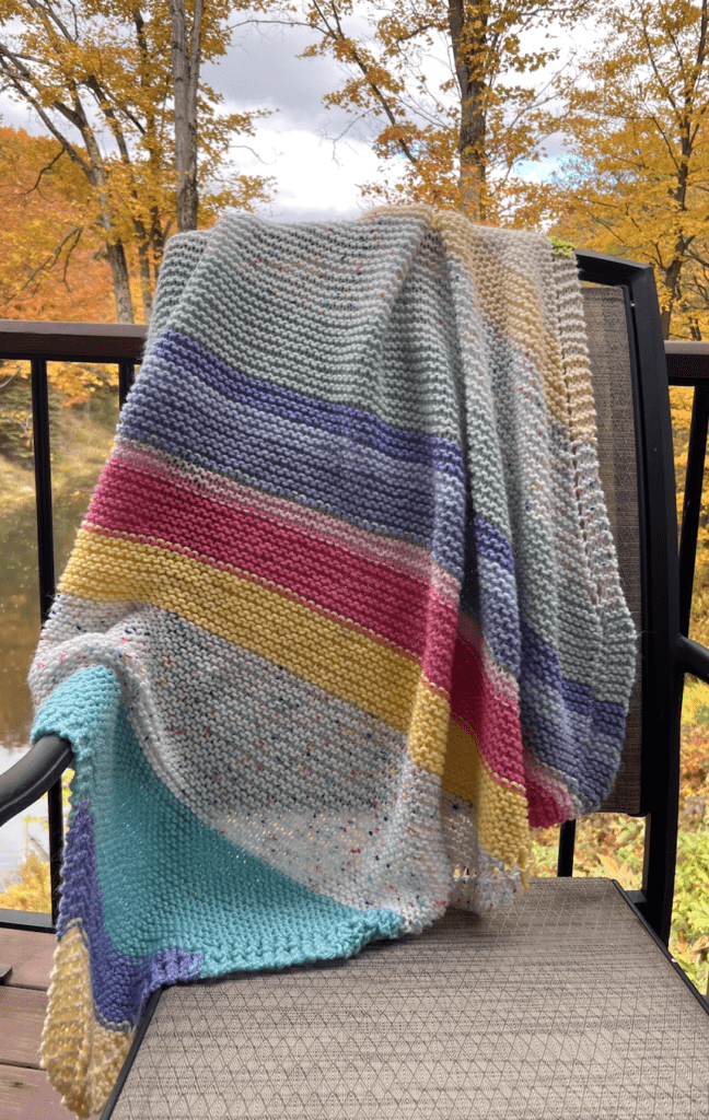 striped handknit baby blanket on chair with fall background