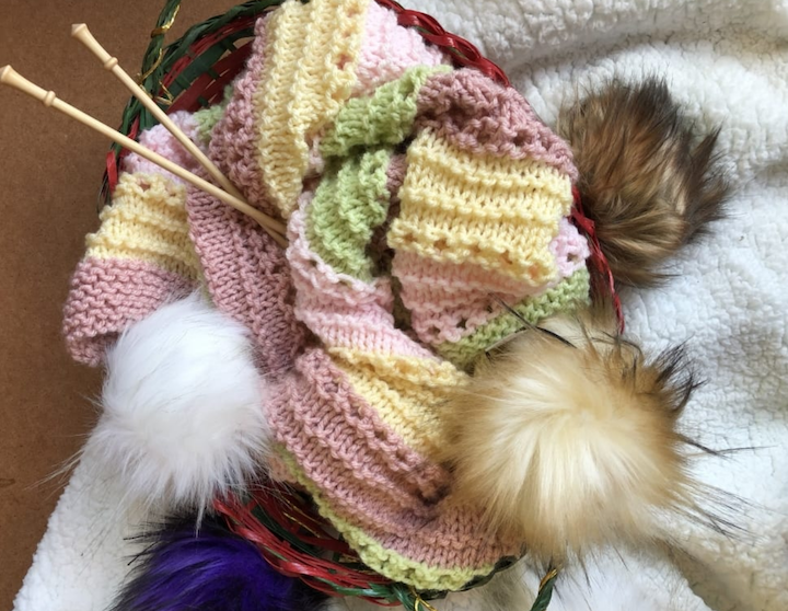 pastel baby blanket with pompoms and knitting needles