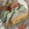 a colorful striped handknit blanket keeping a baby warm in their crib