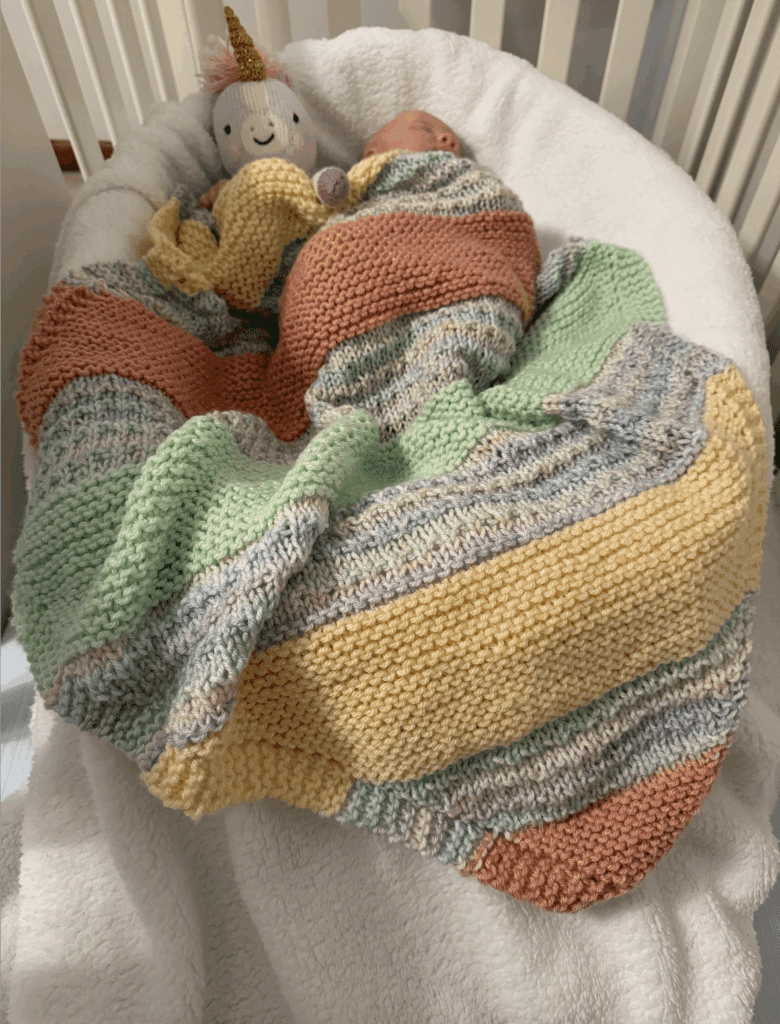a colorful striped handknit blanket keeping a baby warm in their crib