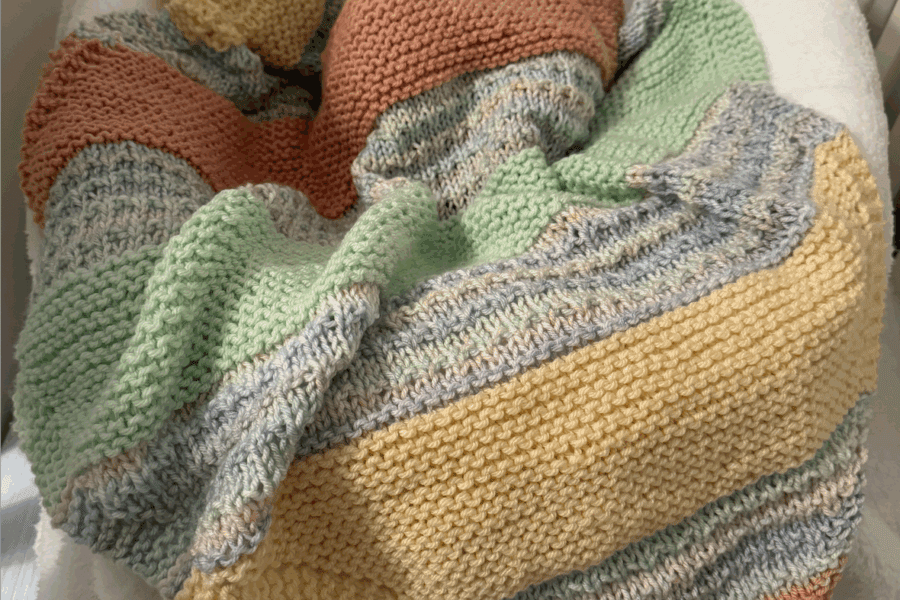 a colorful striped handknit blanket keeping a baby warm in their crib