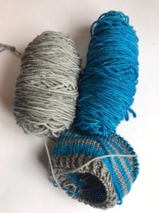 balls of grey and blue yarn and half knitted hat