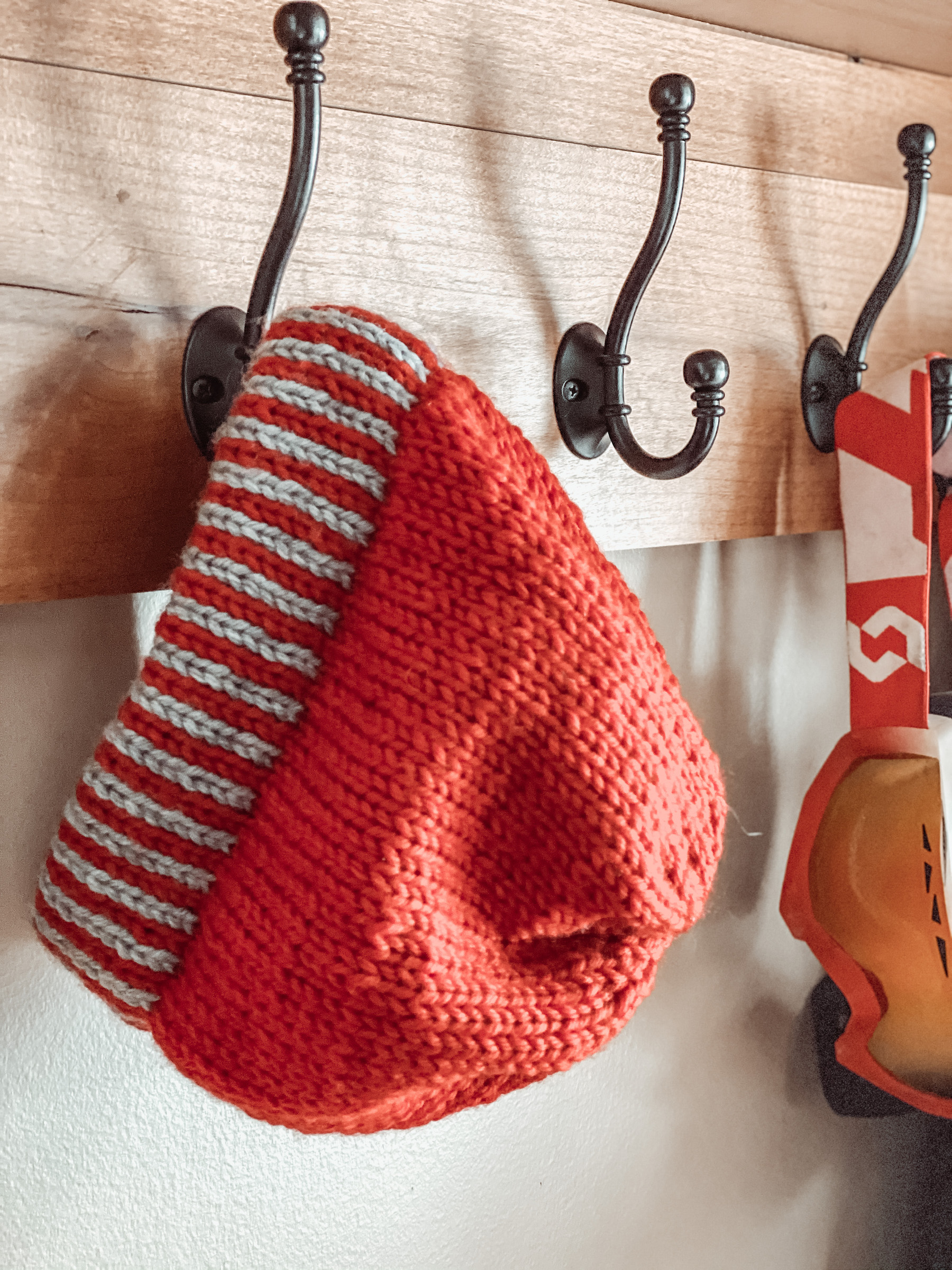 red hat with red/grey striped brim hanging on hook