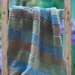 green, gray and blue basketweave style baby blanket on a ladder