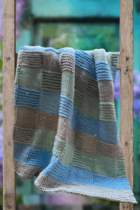 green, gray and blue basketweave style baby blanket on a ladder