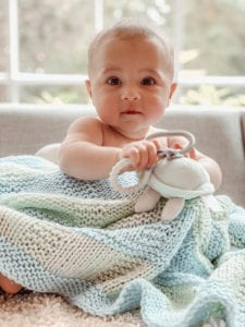 baby with toy and knit blanket