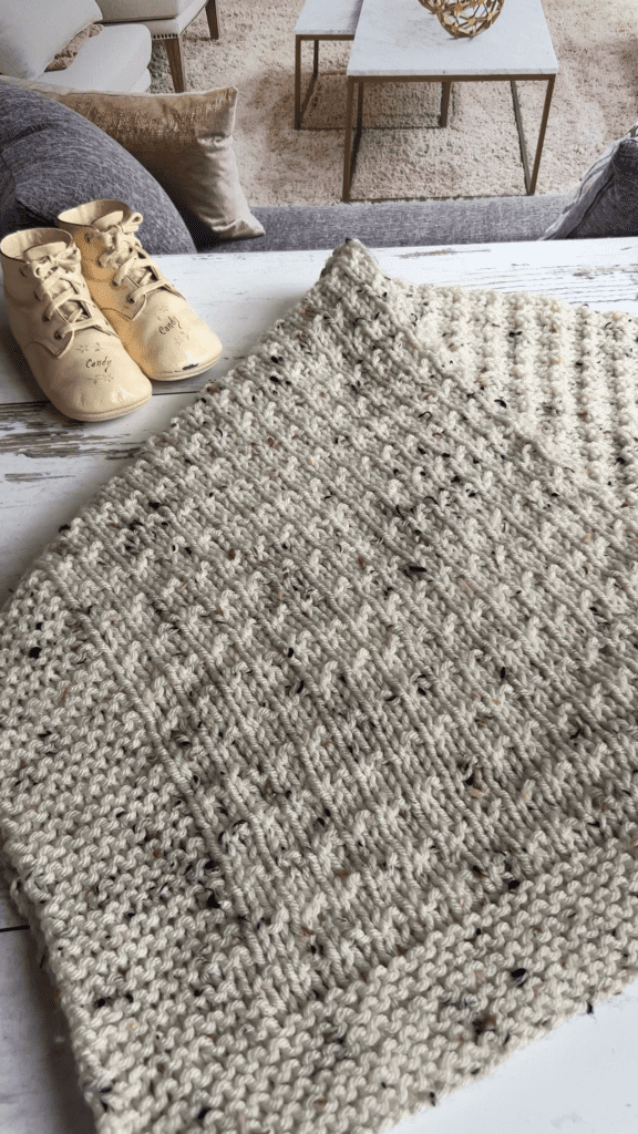 ivory tweed baby blanket folded on table next to baby shoes