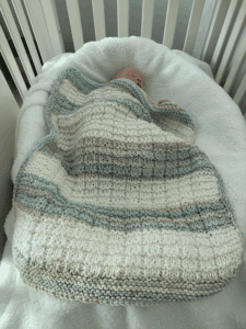 baby sleeping in crib with handknit blanket